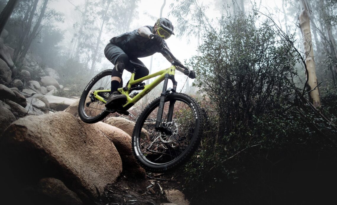 A rider on YT Capra Core 1 drops off of a large rock