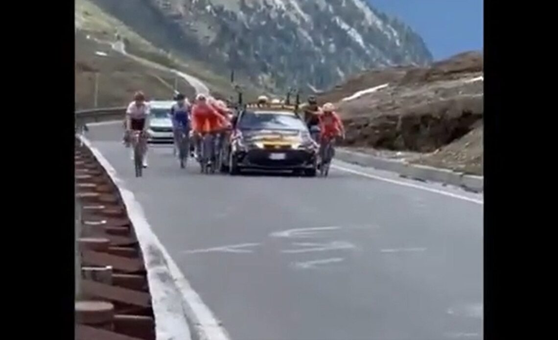 Riders hold onto cars during the Giro Next Gen