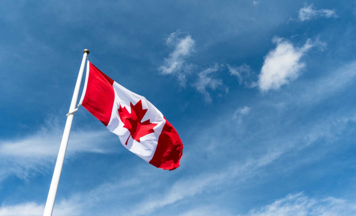 Canada flag pole waving in the wind under beautiful blue sky and clouds wallpaper. Canadian national red maple leaf symbol.