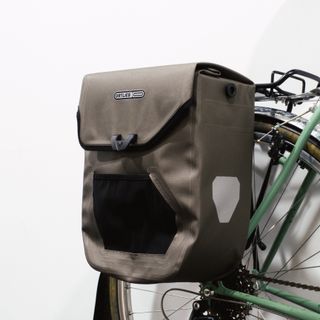 A brown boxy pannier mounted to a green bike against a white background