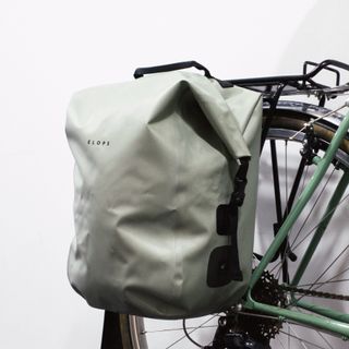 A sage green rolltop pannier mounted to a green bike against a white background