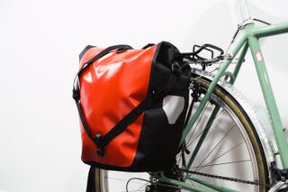 A bright red pannier mounted to a green bike against a white background