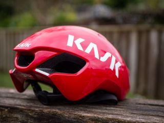 A red Kask Utopia Y aero helmet sits on a wooden bench