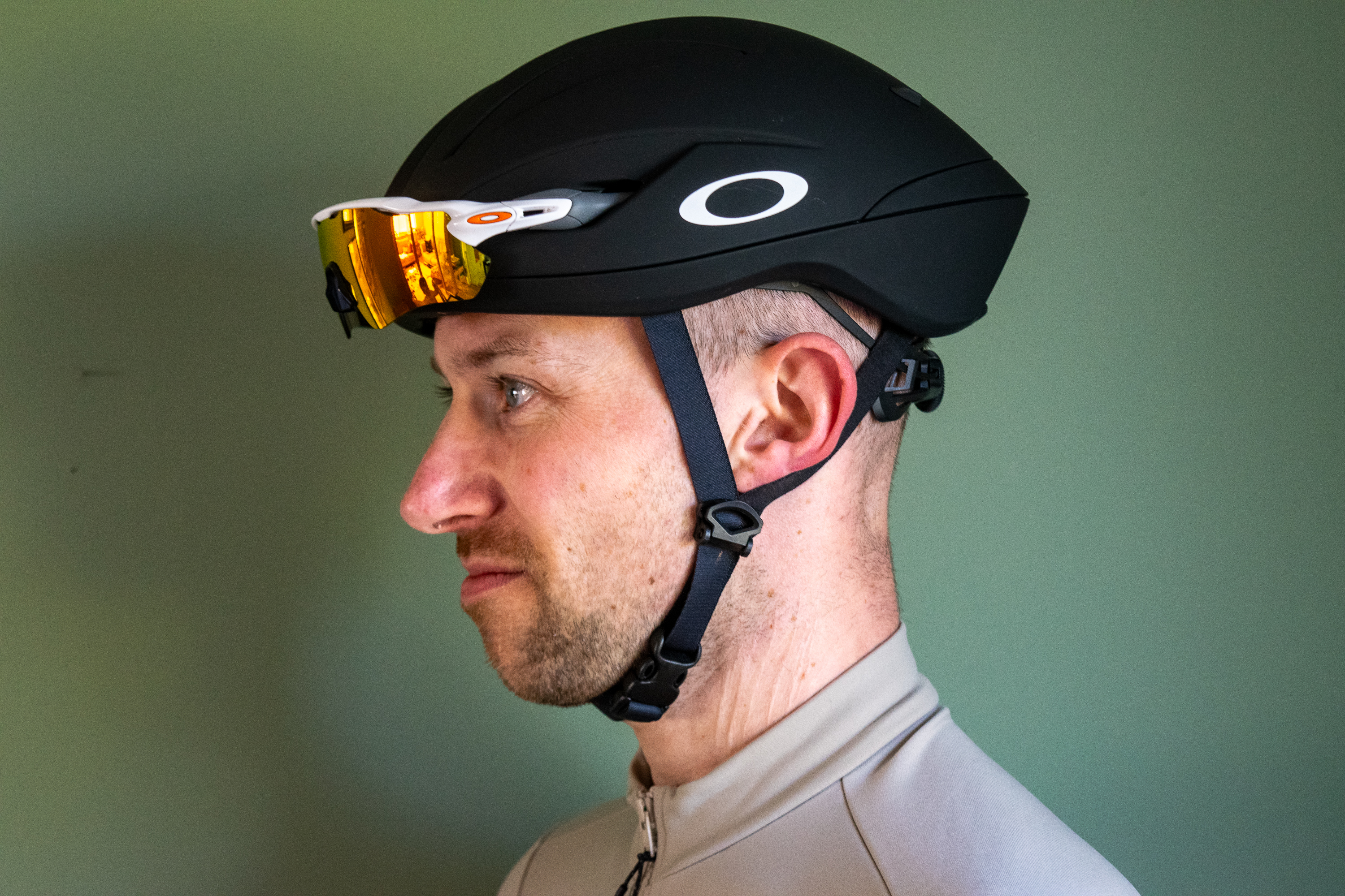 A rider wearing a black Oakley Velo Mac helmet in front of a green wall 
